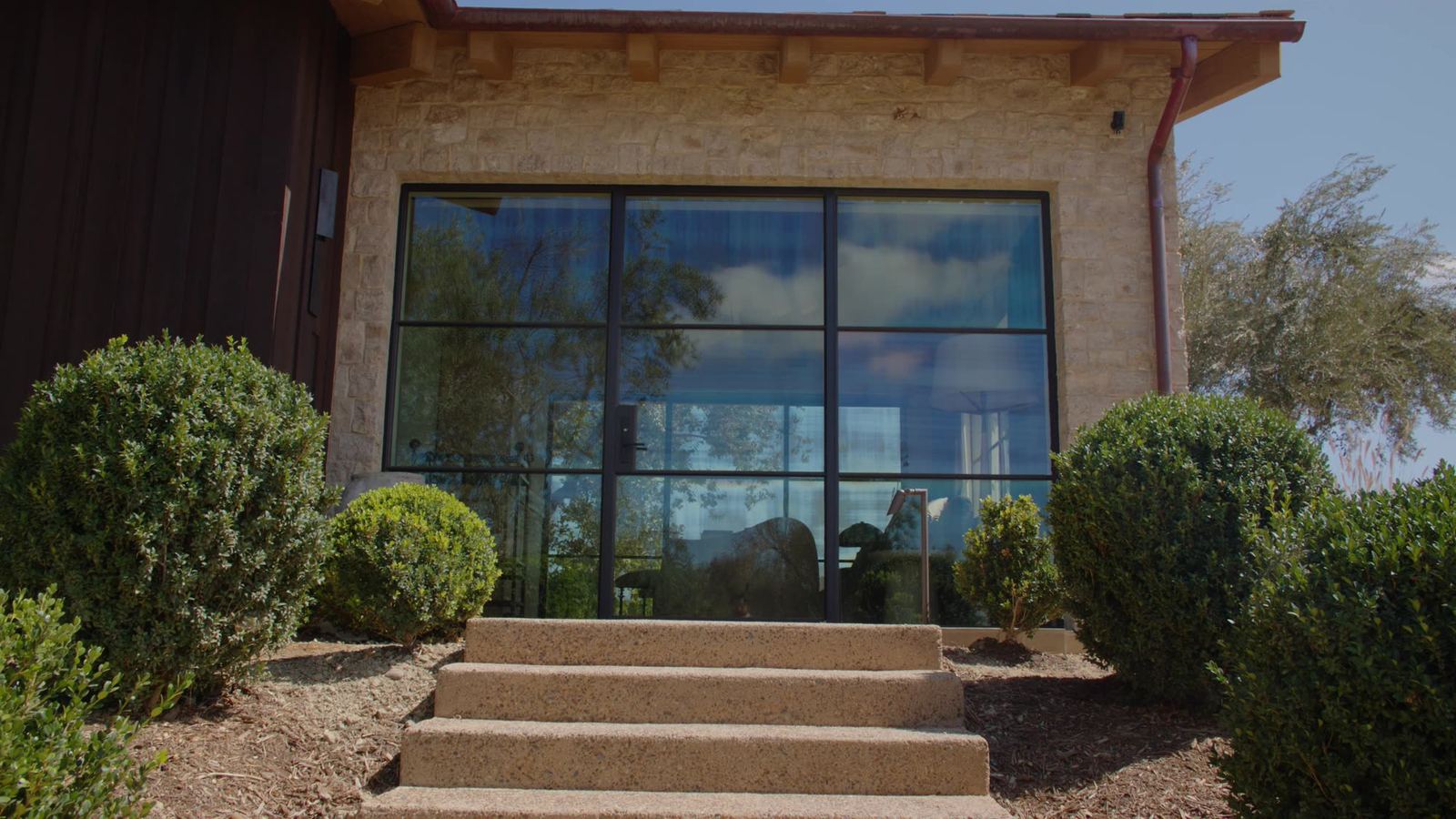 Stone and vertical siding meeting a full-height glass wall above poured entry steps