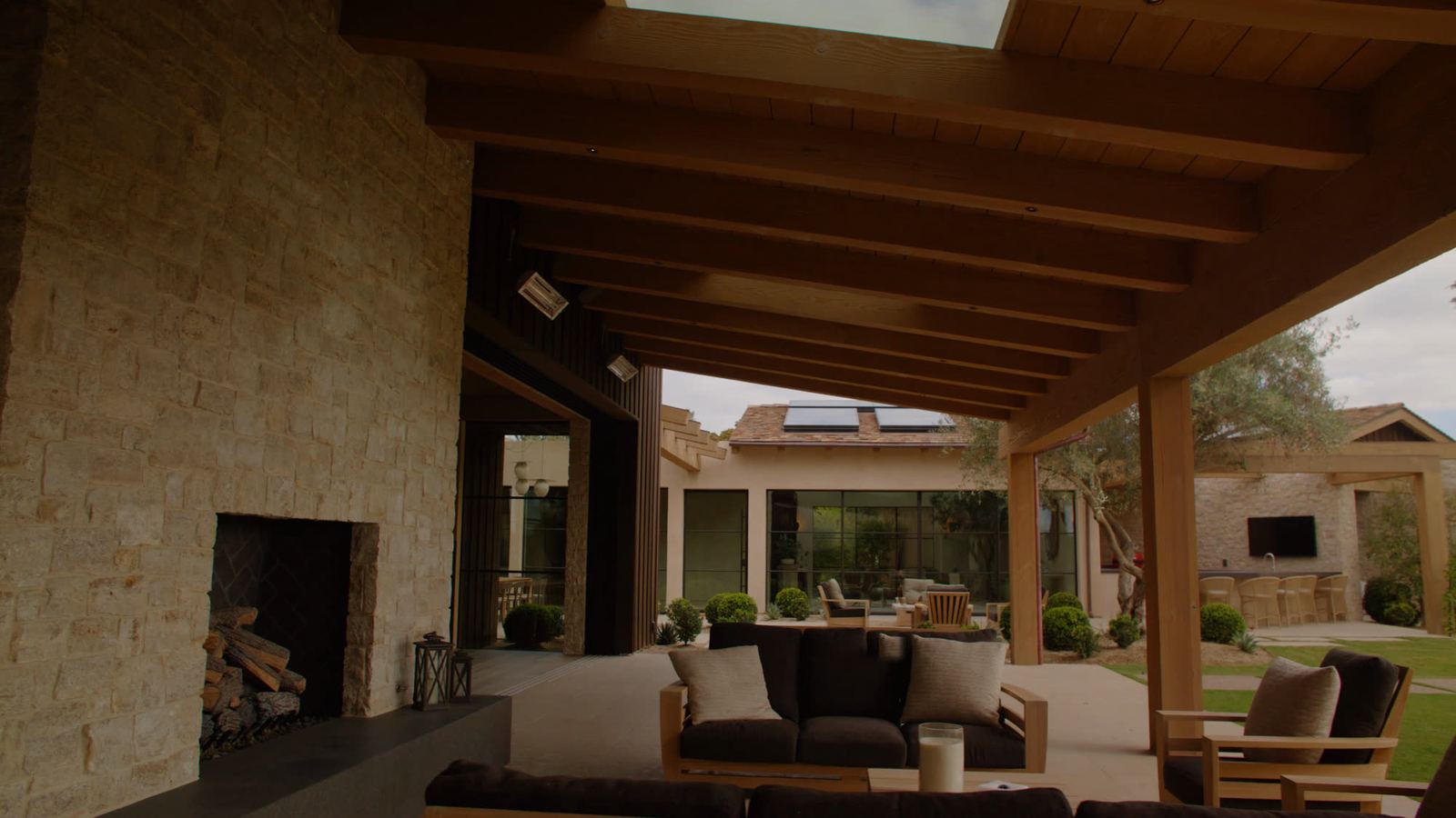 Outdoor room with exposed timber ceiling, stone fireplace and concrete floor